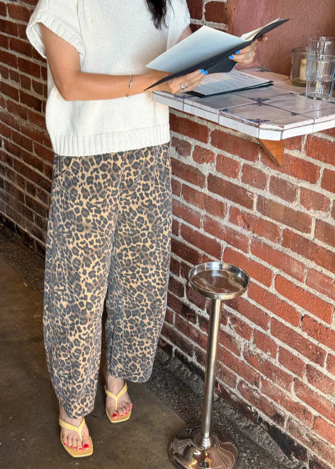 Person wearing leopard print pants and a white top, standing near a brick wall.