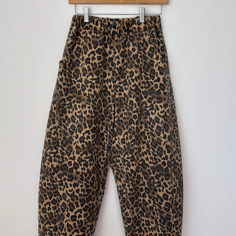 Leopard print pants hanging on a wooden hanger against a white background