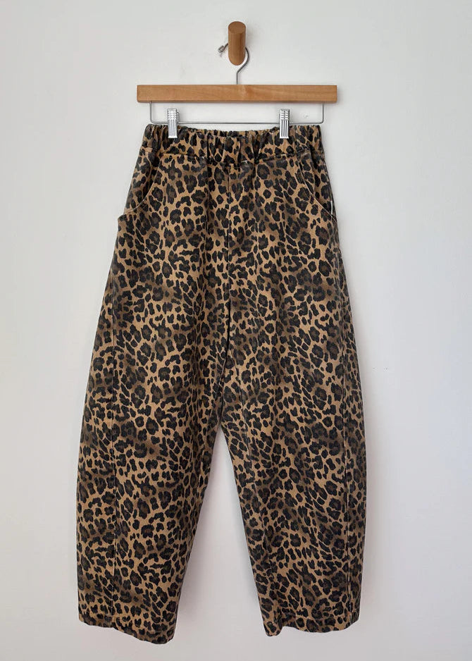Leopard print pants hanging on a wooden hanger against a white background