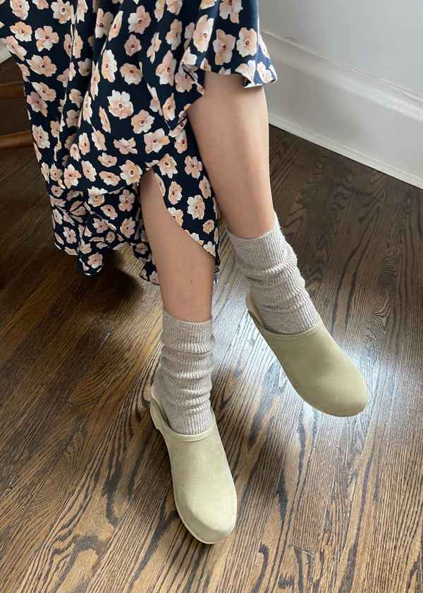 Person wearing a floral dress, gray socks, and light green shoes on a wooden floor.