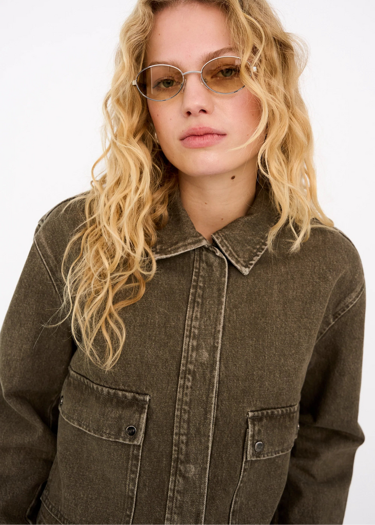 Woman wearing a brown jacket and sunglasses against a white background