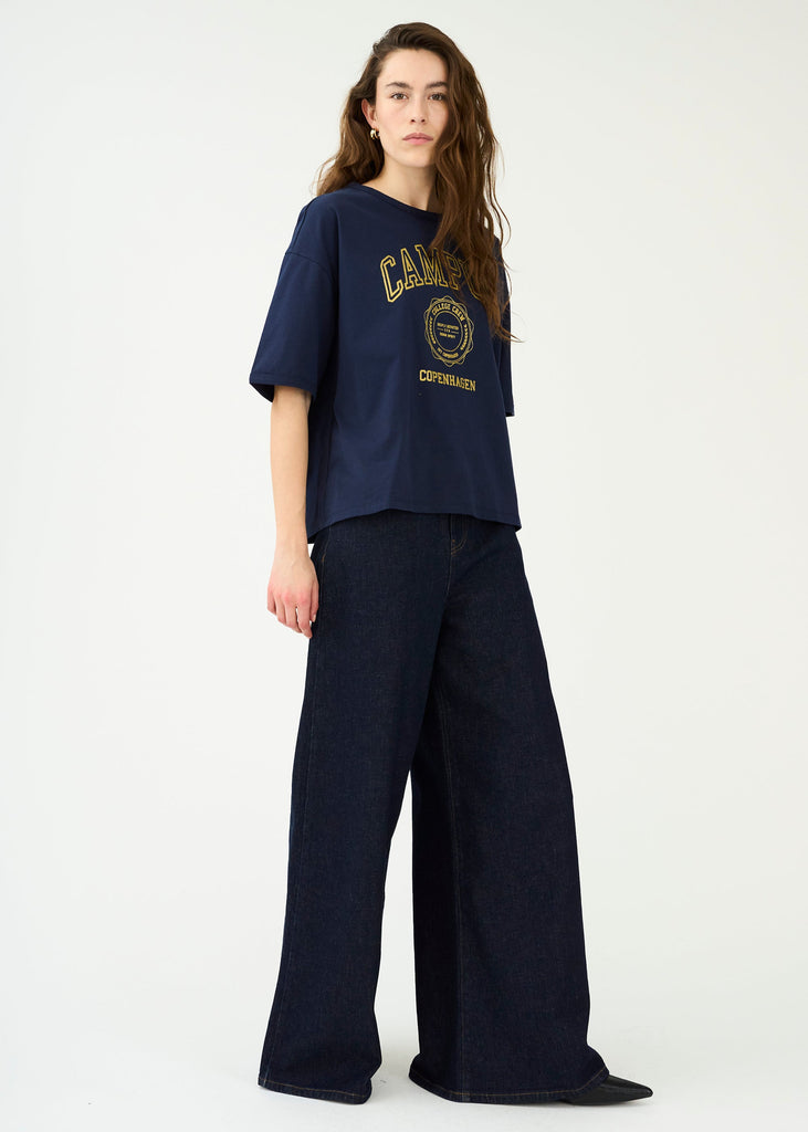 Person wearing a navy blue t-shirt with a logo and wide-leg jeans on a white background