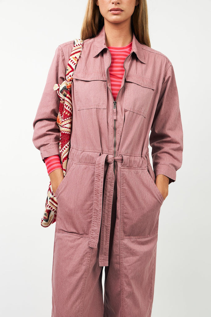 Person wearing a pink jumpsuit with a striped shirt underneath, holding a patterned bag.