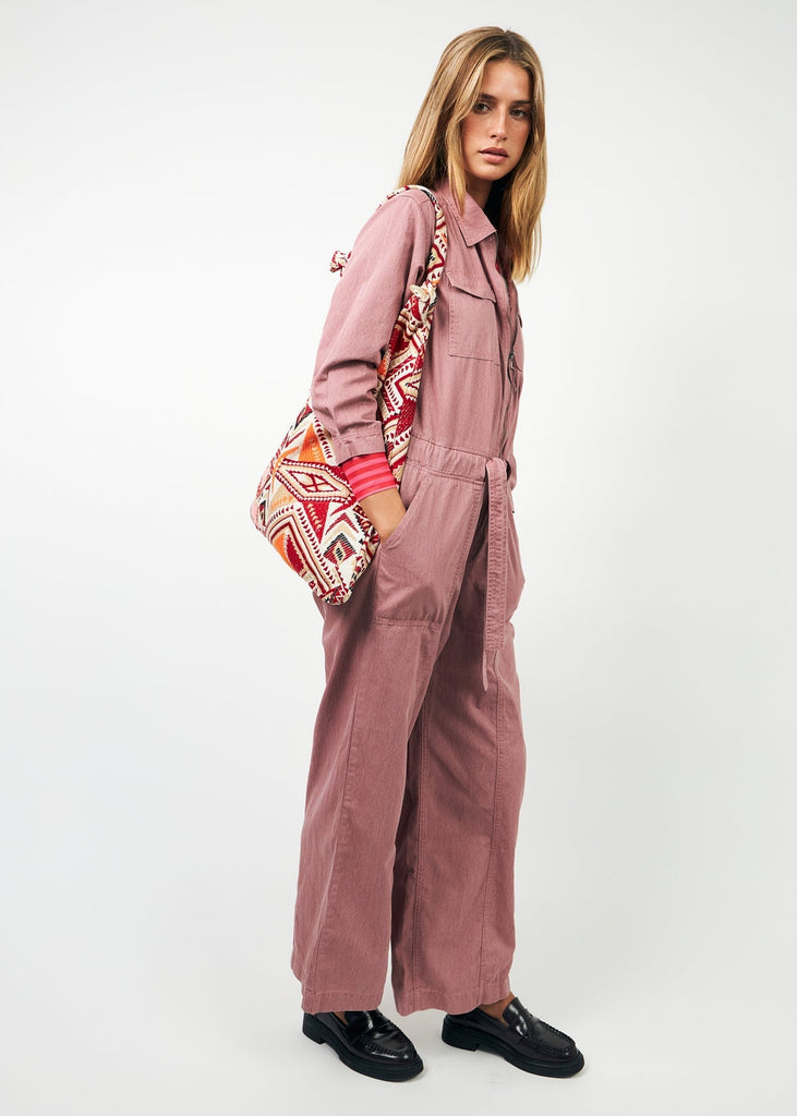 Woman wearing a pink jumpsuit with a patterned bag on a white background