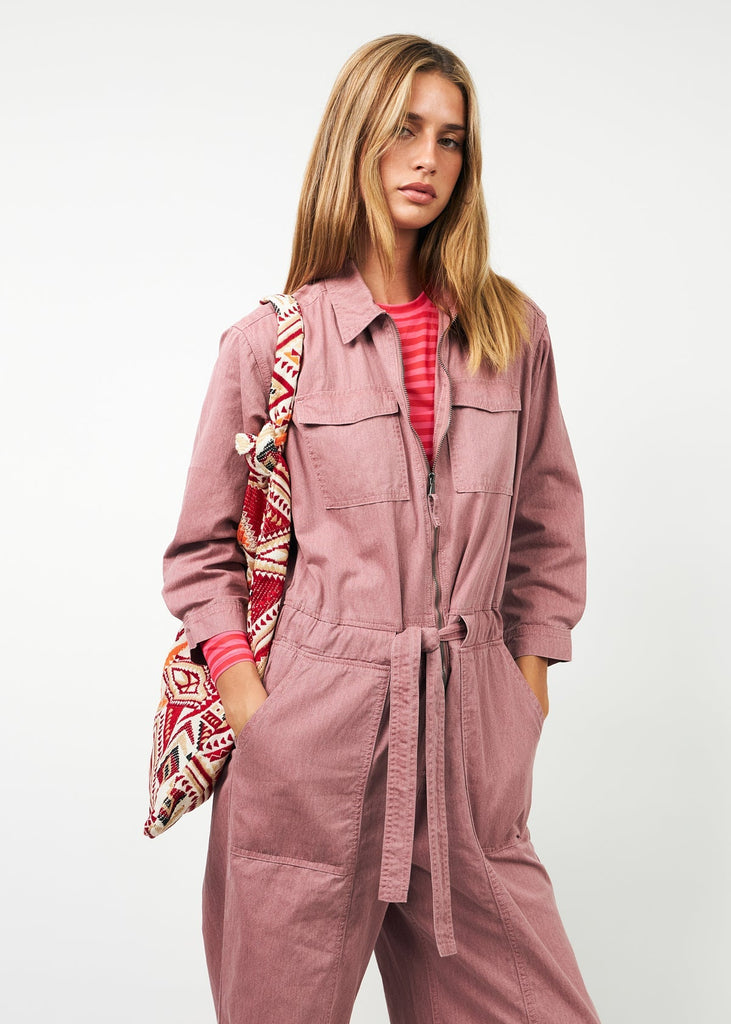 Woman wearing a pink jumpsuit holding a patterned bag against a white background