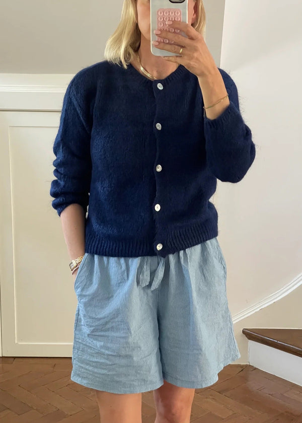 Person wearing a navy cardigan and light blue shorts taking a mirror selfie.