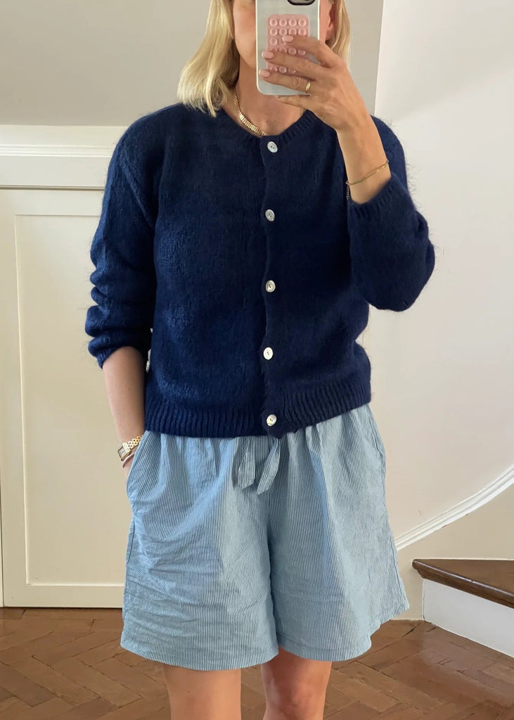 Person wearing a navy cardigan and light blue shorts taking a mirror selfie.