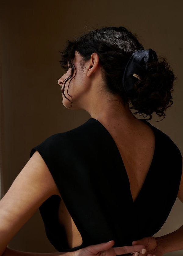 Woman wearing a black dress with a deep neckline against a plain background