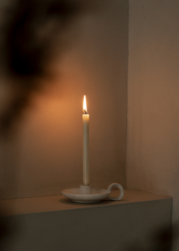 Candle in a white holder on a beige surface with a blurred background