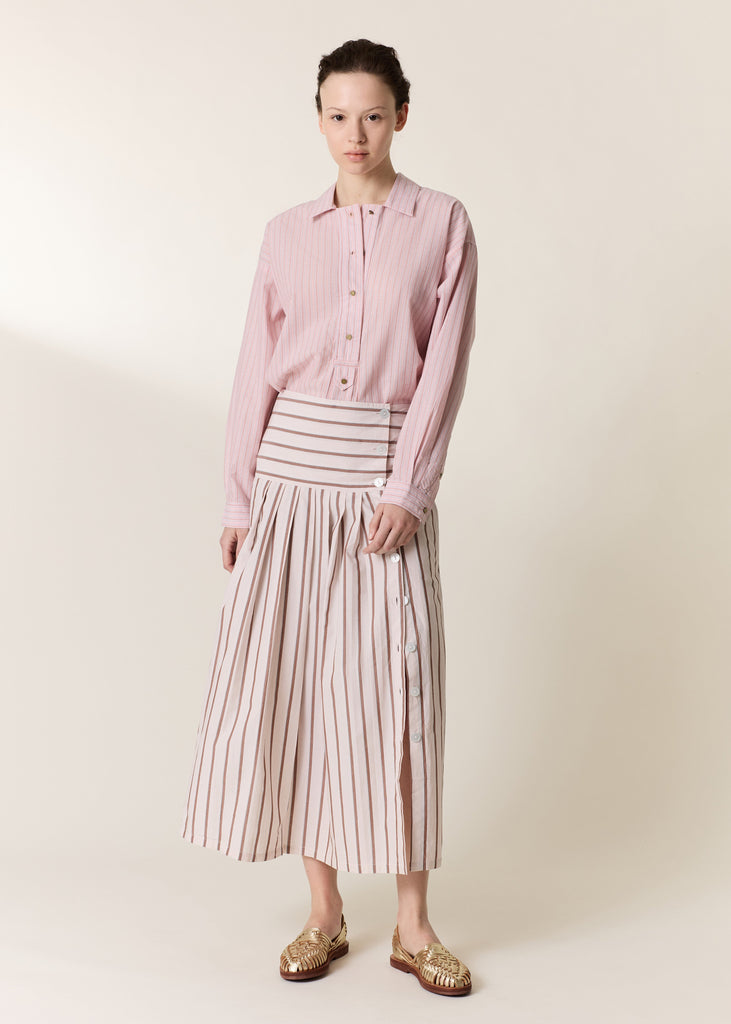 Woman wearing a pink shirt and striped skirt on a plain background