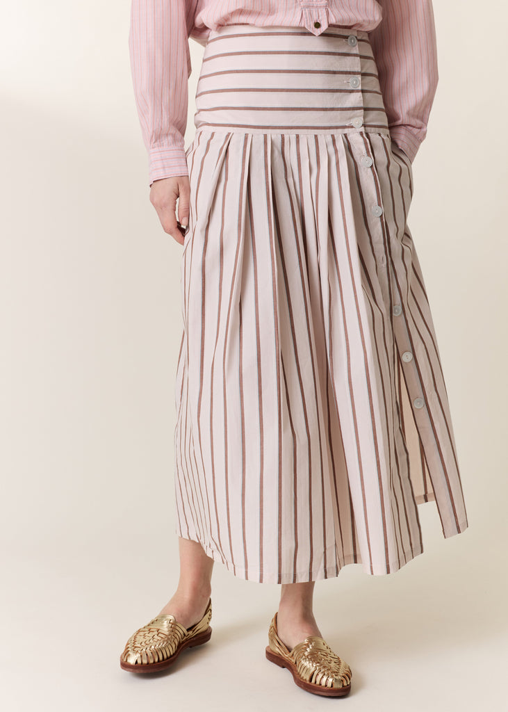 Person wearing a pink shirt and striped skirt on a plain background