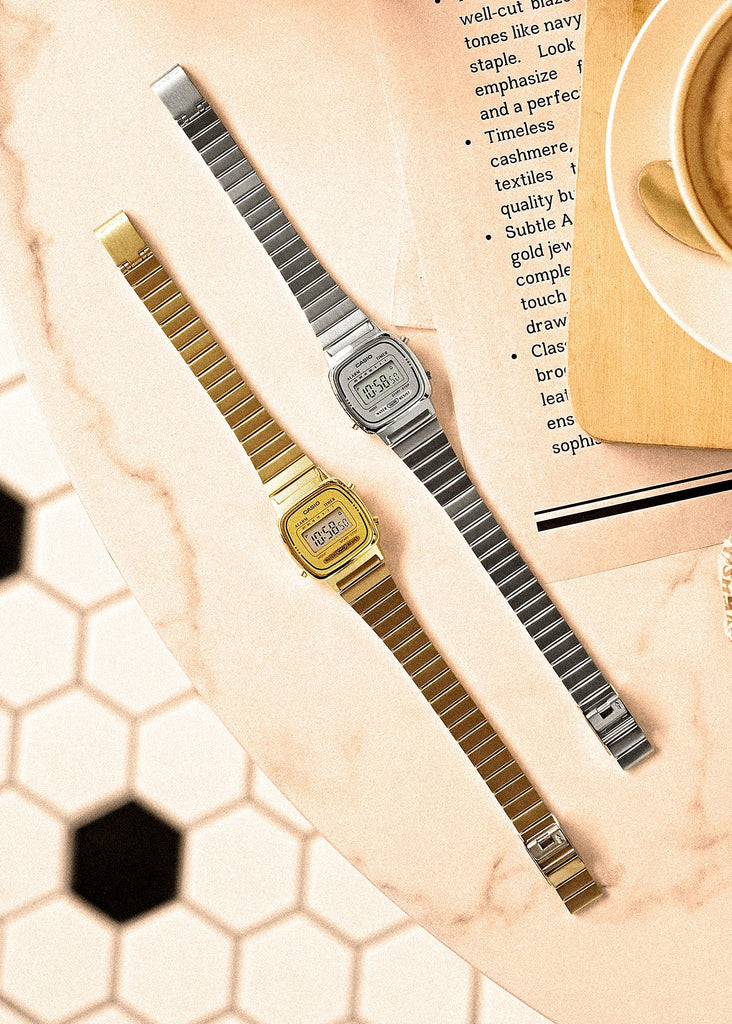 Two vintage-style digital watches with metal straps on a textured surface.