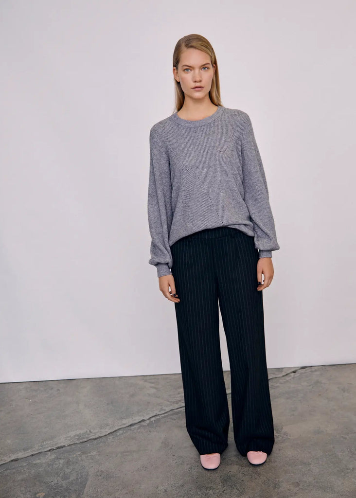 Woman wearing a gray sweater and black pinstripe pants against a white background