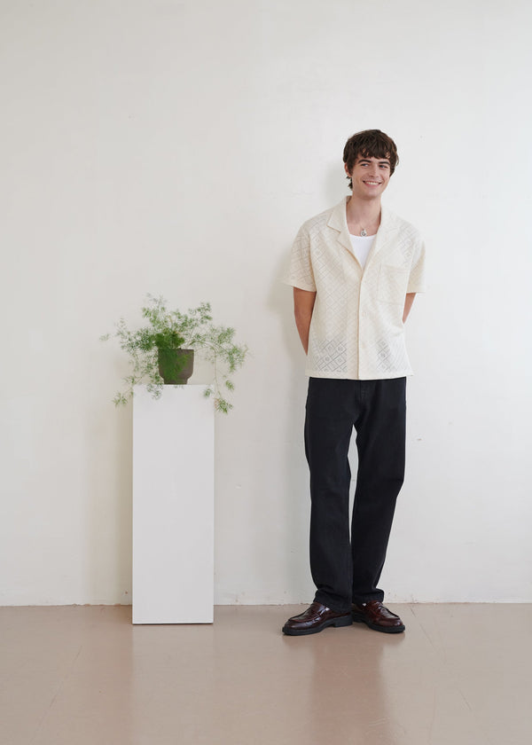 Person standing in a minimalistic room with a white wall and a small plant on a pedestal.