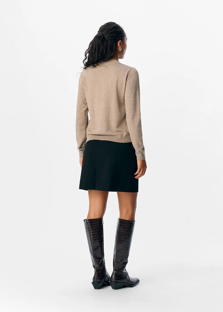 Woman wearing a beige sweater and black skirt with knee-high boots on a white background