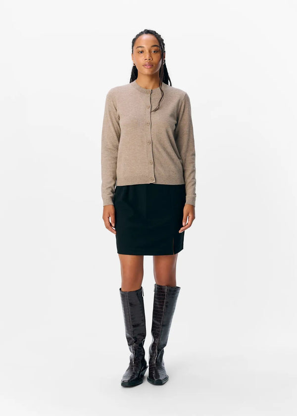 Woman wearing a beige shirt, black skirt, and black knee-high boots on a white background