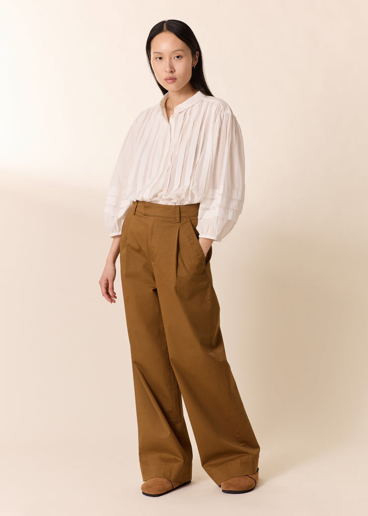Woman wearing a white blouse and brown pants against a beige background