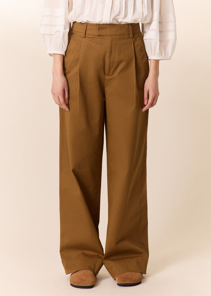 Person wearing brown wide-leg pants and a white blouse on a beige background