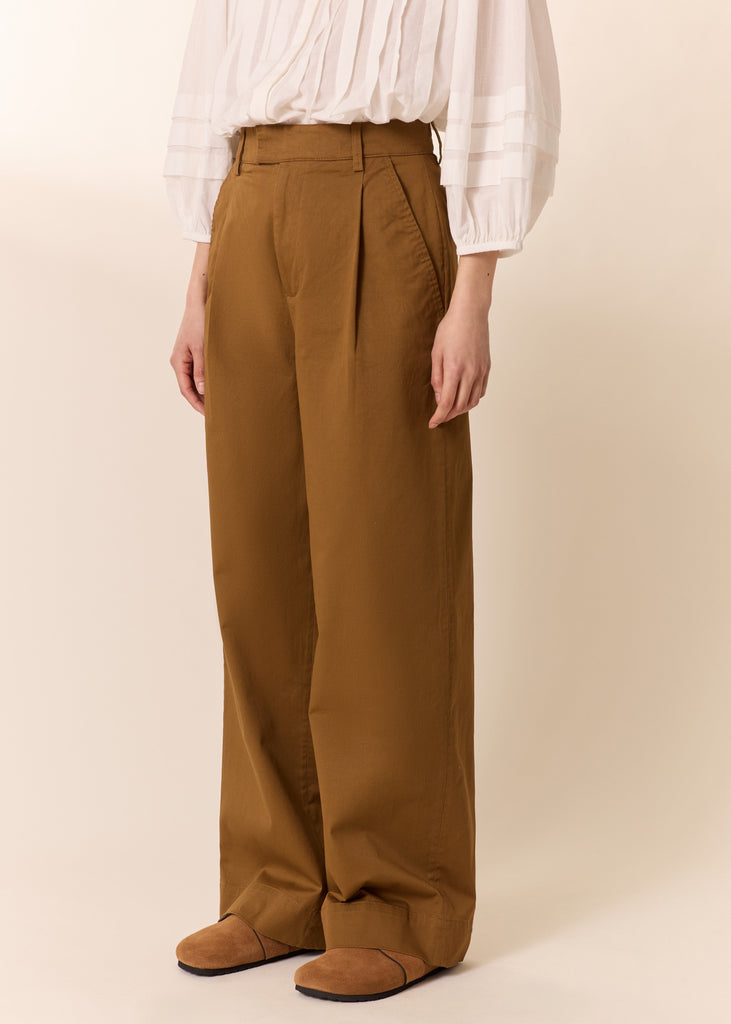 Person wearing brown pants and a white blouse on a beige background