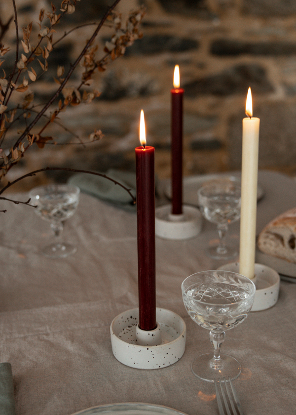 Candlelit table setting with candles, glasses, and bread on a stone wall background.