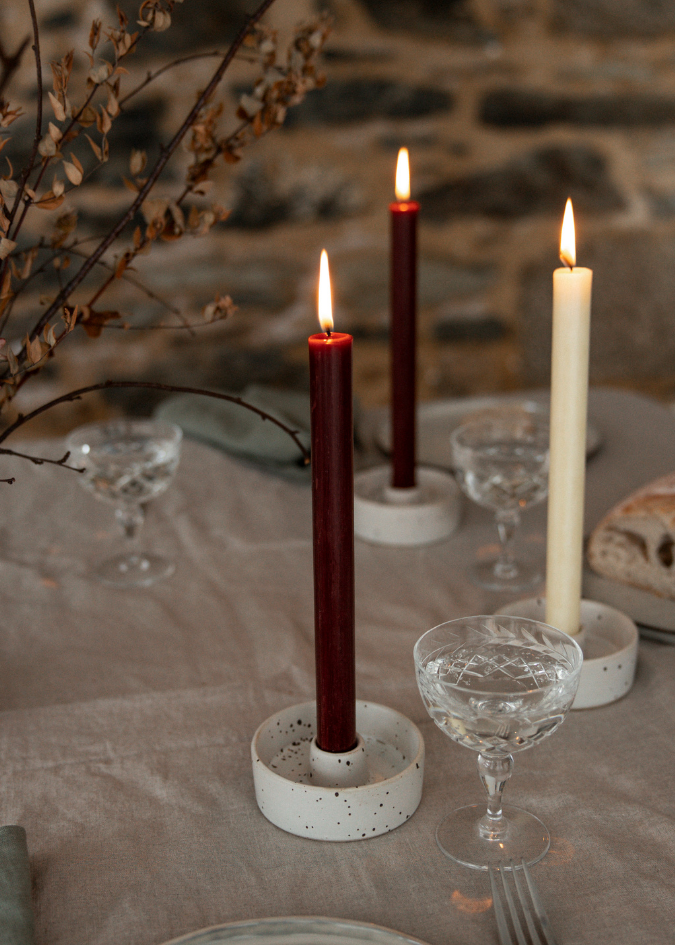 Candlelit table setting with candles, glasses, and bread on a stone wall background.
