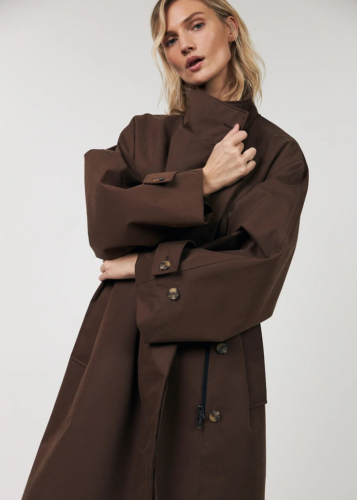 Woman wearing a brown trench coat against a white background