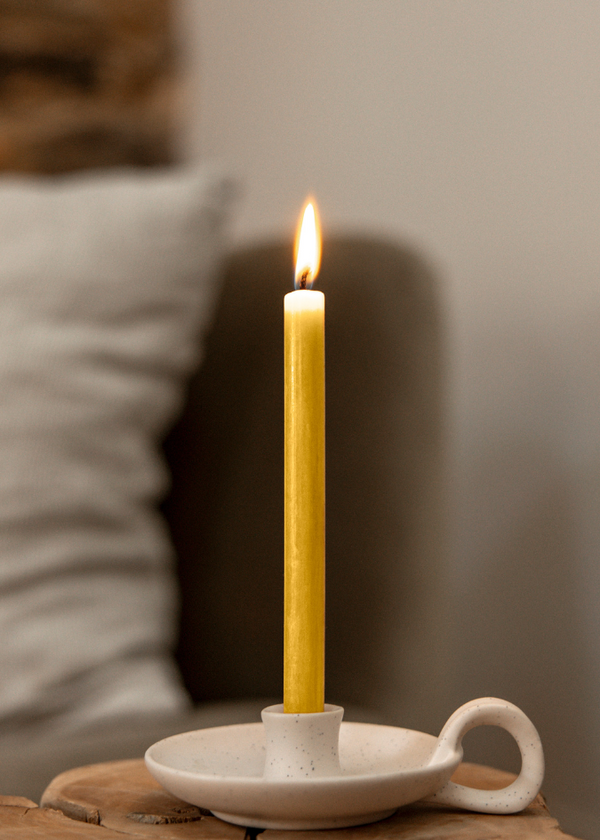 Yellow candle in a white ceramic holder on a wooden surface with a blurred background
