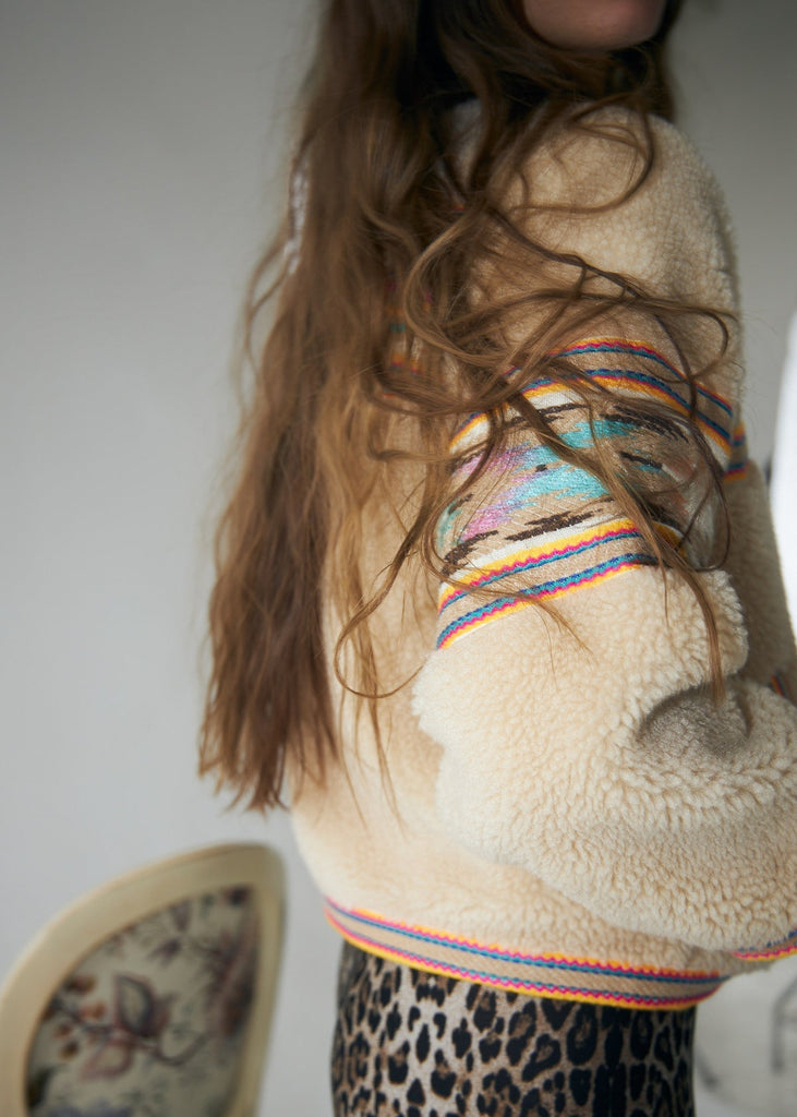 Person wearing a colorful striped sweater with a fluffy texture, standing against a neutral background.