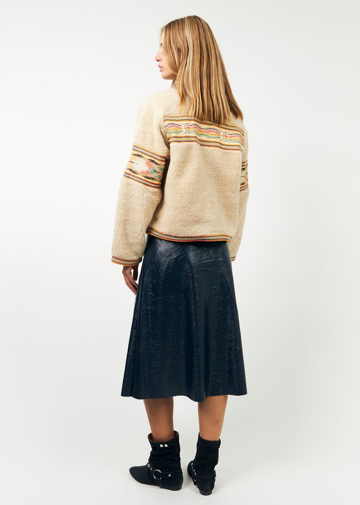 Person wearing a beige sweater with patterned sleeves and a black skirt on a white background