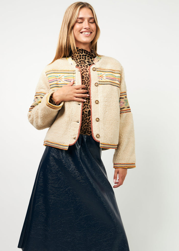 Woman wearing a patterned jacket over a leopard print top and dark blue skirt on a white background