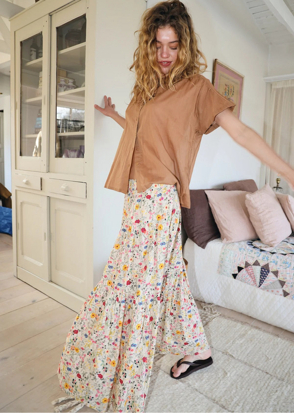 Woman in a living room wearing a brown top and floral skirt.