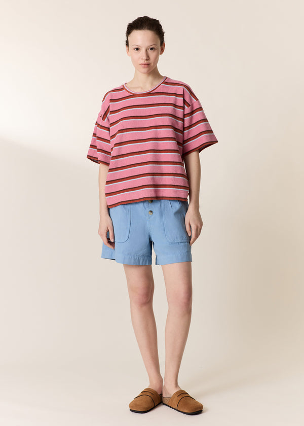 Person wearing a pink and brown striped shirt with light blue shorts on a beige background