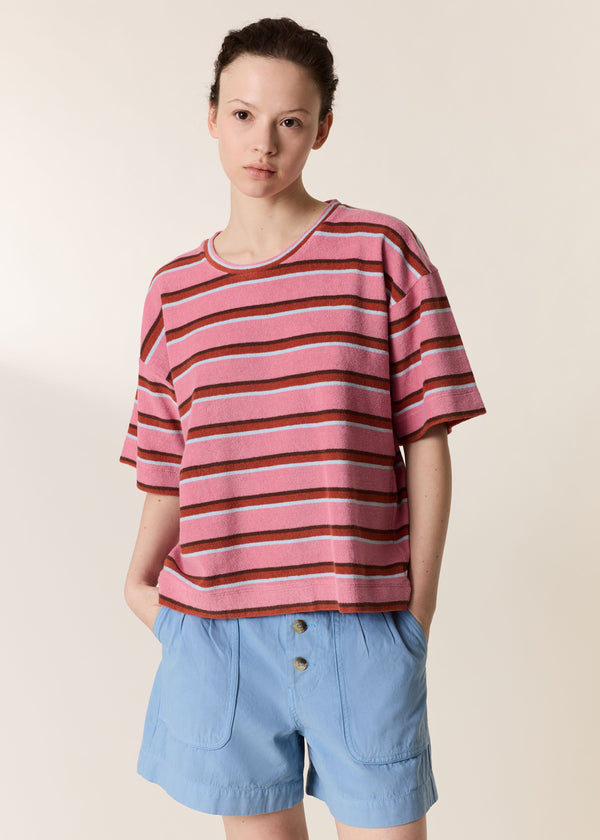 Person wearing a pink and brown striped shirt with light blue shorts on a beige background