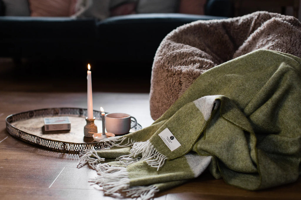 Green blanket with a label on a wooden surface next to a candle and mug.