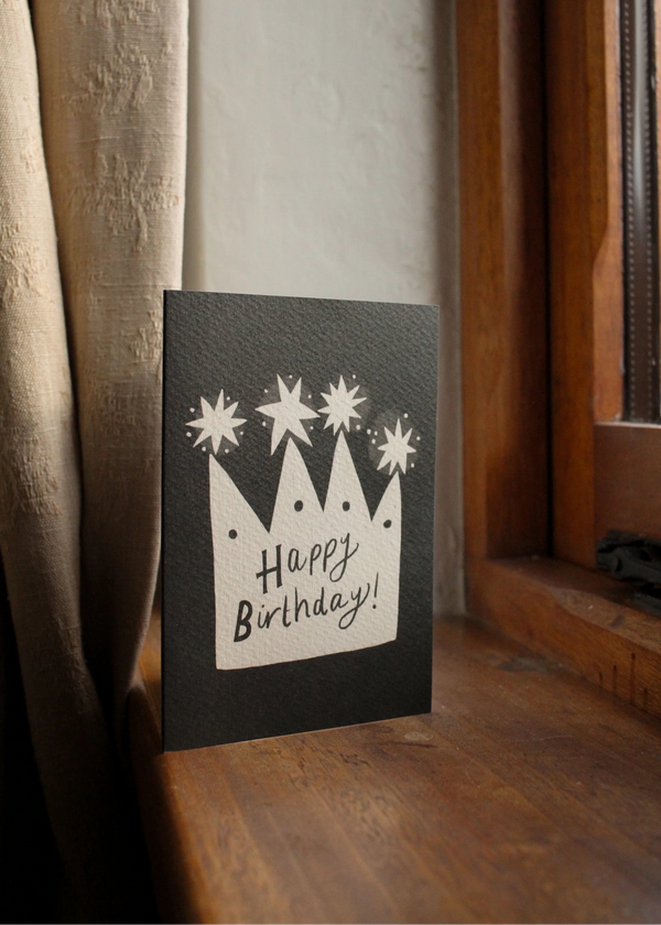 Black birthday card with white text and stars on a wooden surface.