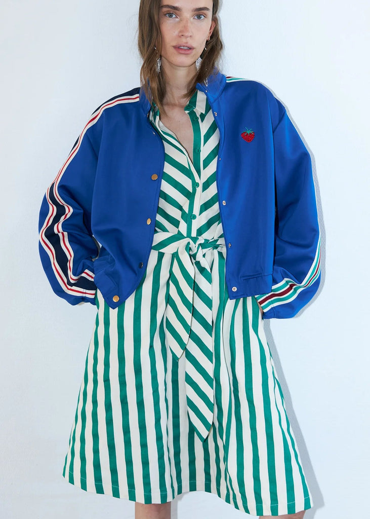Woman wearing a blue jacket with red heart detail and a green and white striped dress on a white background