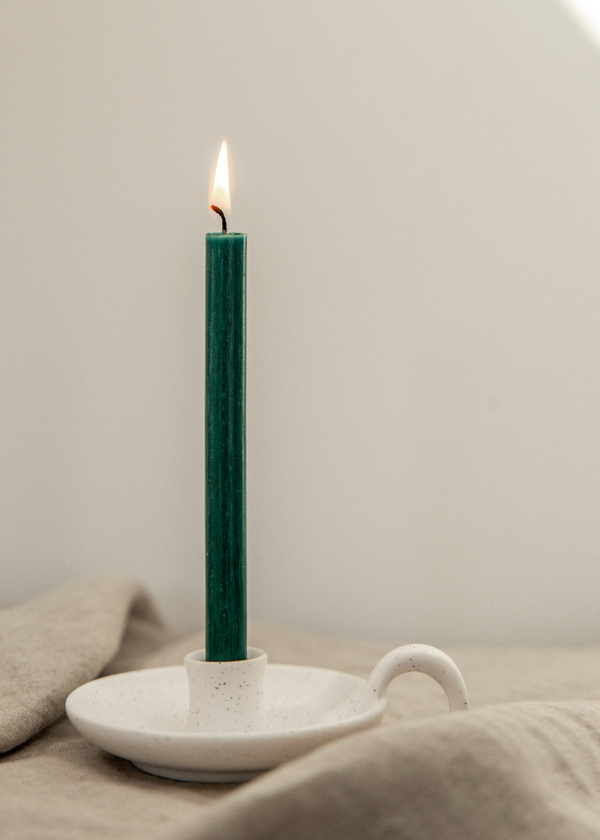 Green candle in a white ceramic holder on a neutral background