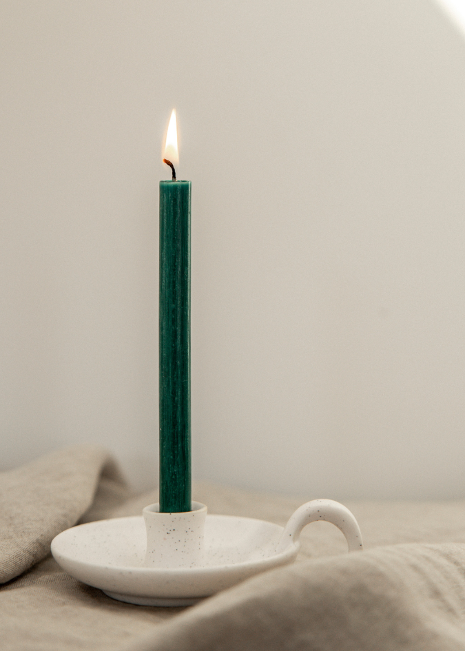Green candle in a white ceramic holder on a neutral background