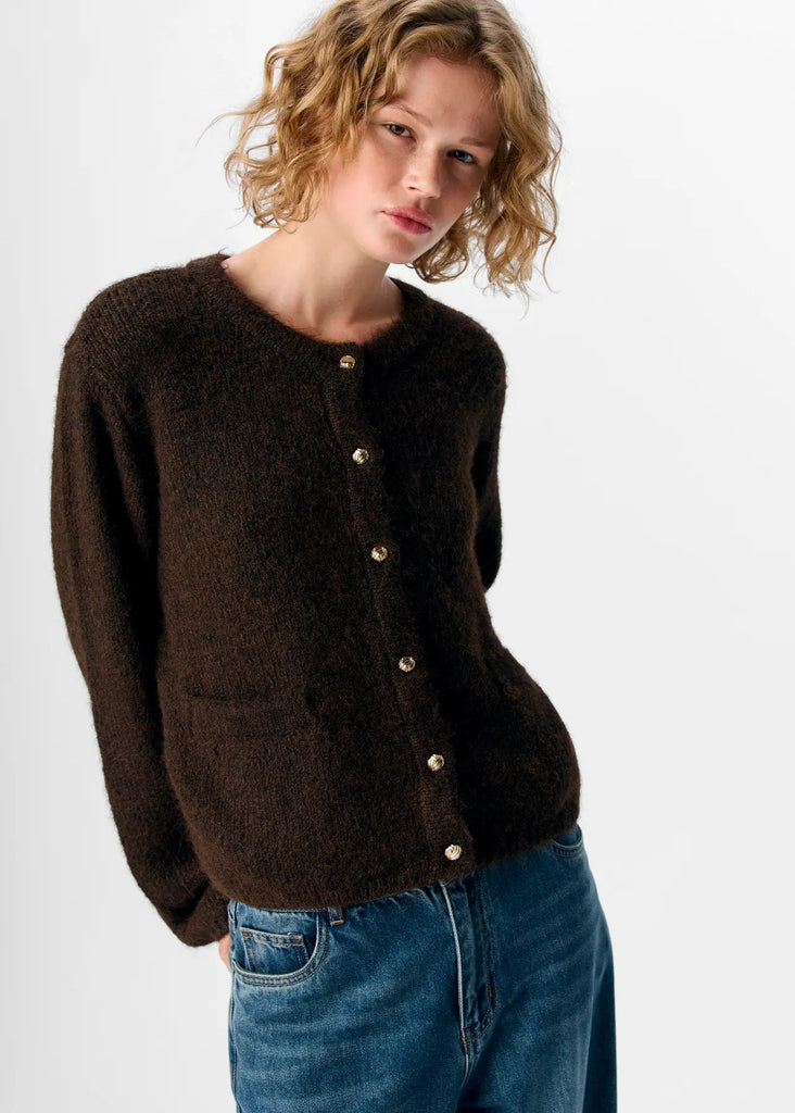 Person wearing a brown cardigan with gold buttons on a white background