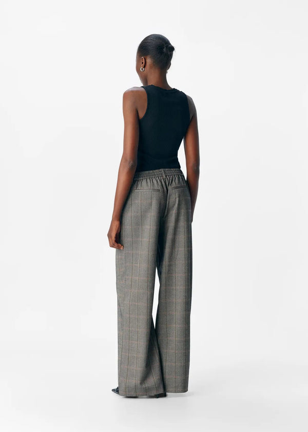 Person wearing a black sleeveless top and plaid pants on a white background