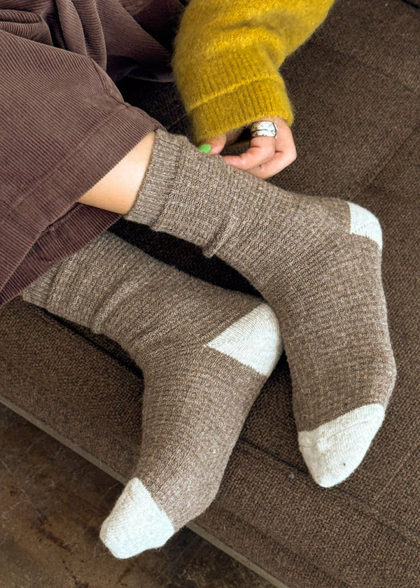 Person wearing brown socks with white toes and heels on a brown couch.