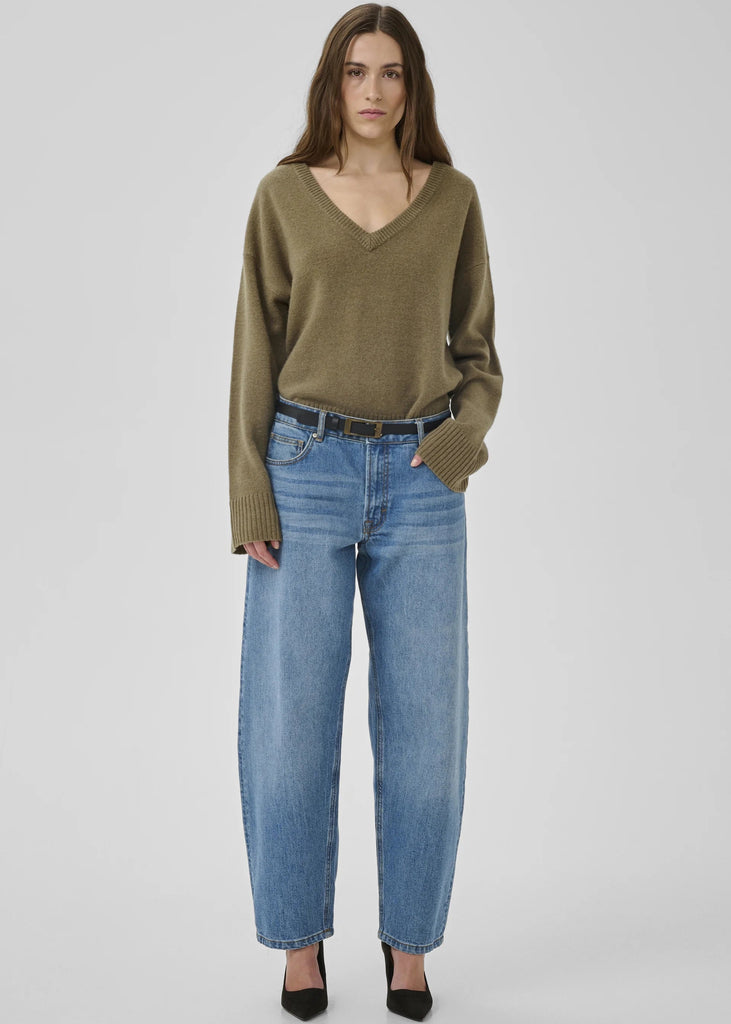 Woman wearing a green sweater and blue jeans on a white background