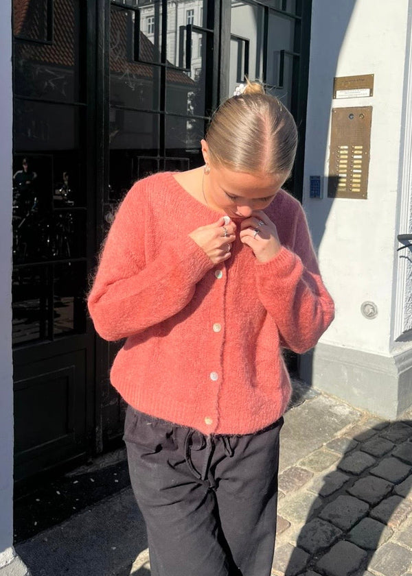 Person wearing a red sweater and black pants standing on a street.