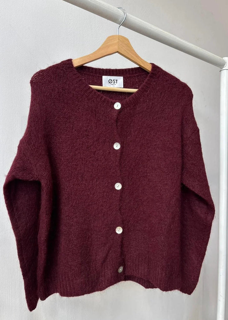 Maroon cardigan on a hanger against a white background