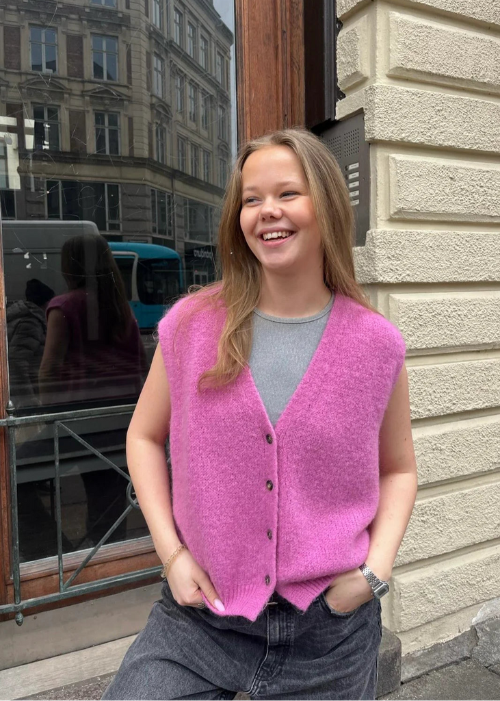 Person wearing a pink vest standing outside a building with a reflective surface.