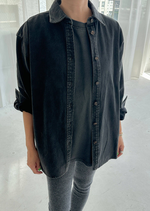 Person wearing a dark denim jacket over a plain shirt and gray pants in a minimalistic setting.