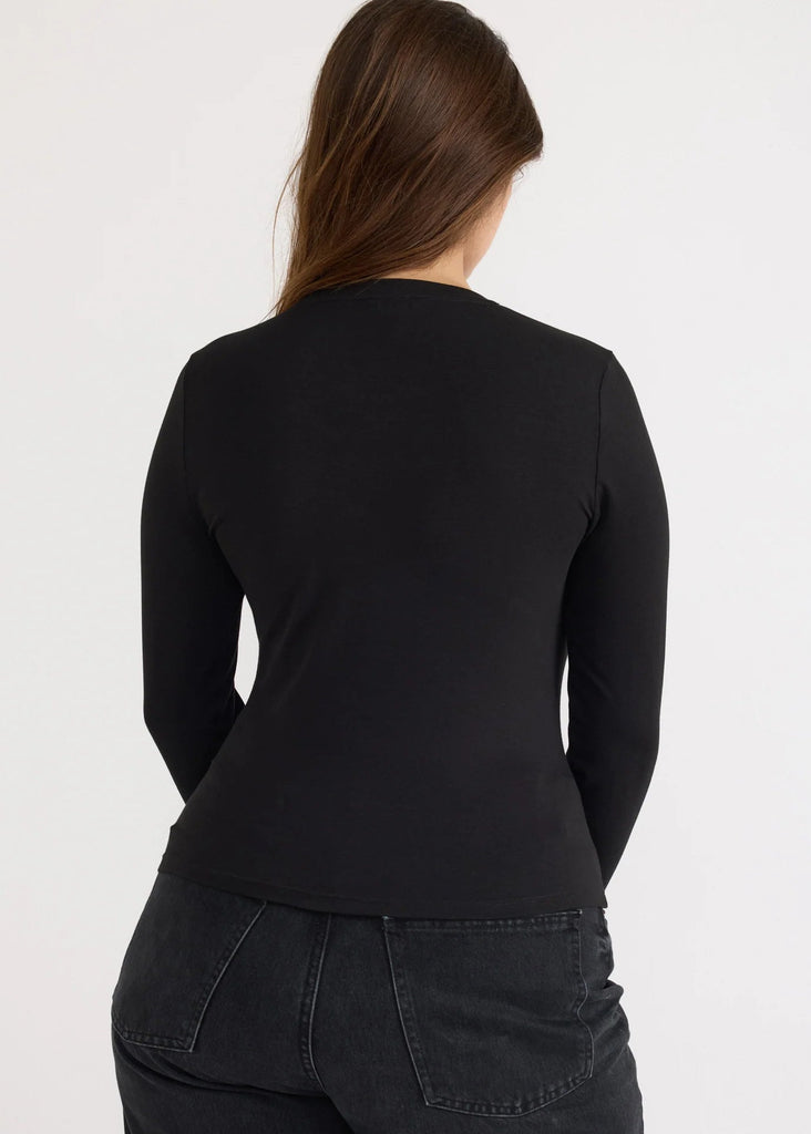 Person wearing a black long-sleeve top and dark jeans on a white background