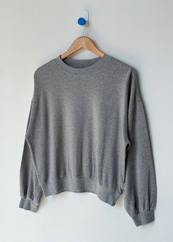Gray sweatshirt on a wooden hanger against a white wall