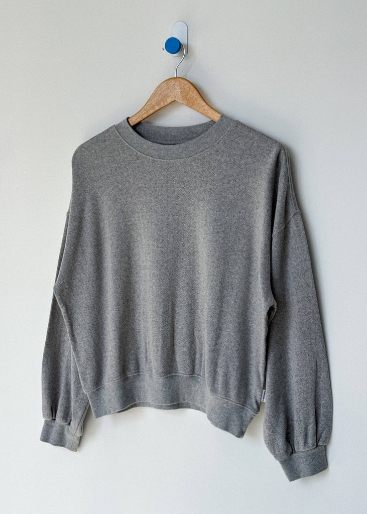Gray sweatshirt on a wooden hanger against a white wall