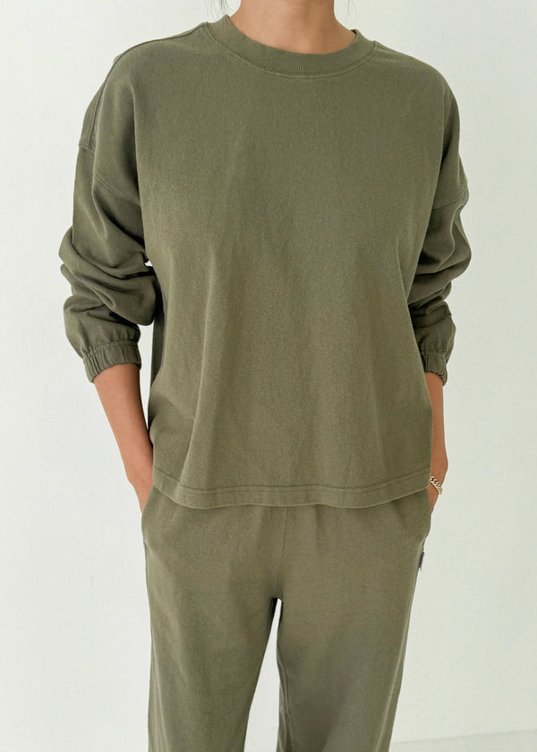 Person wearing an olive green sweatshirt and pants on a white background